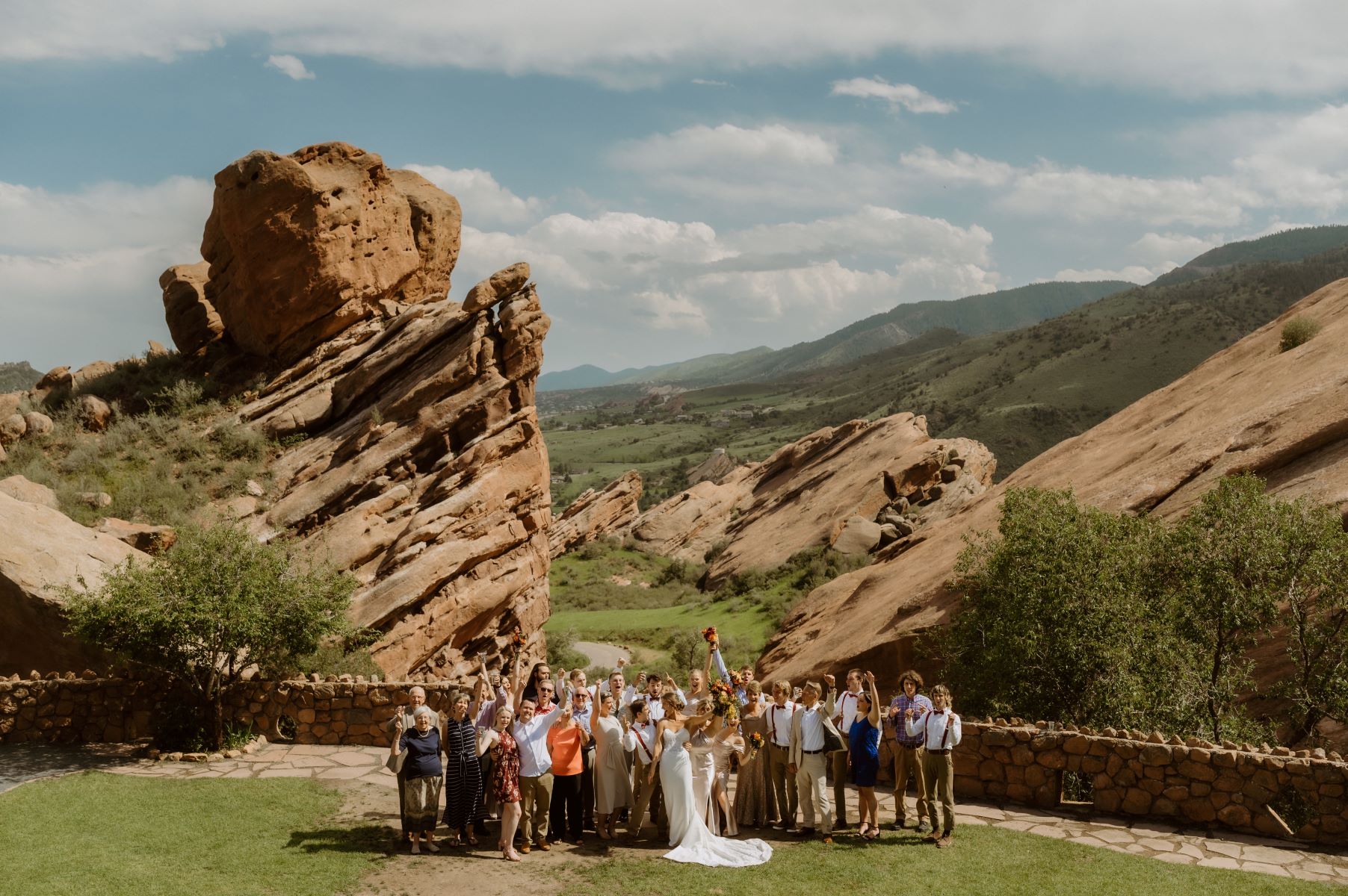 A couple celebrating their marriage and behind them their wedding party is cheering and behind them are red rock formations and mountains 