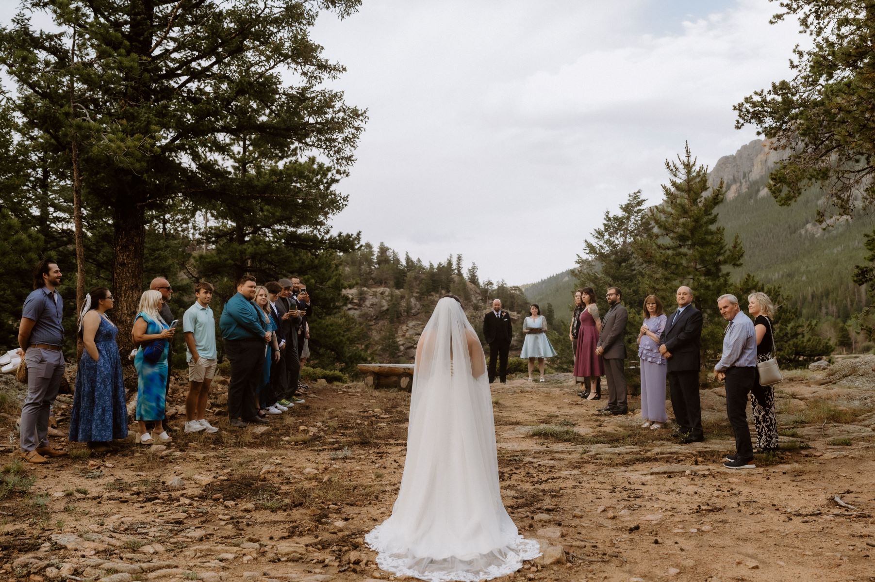 A woman walking down a dirt path in her wedding dress to her partner for their wedding ceremony as their guests watch her 