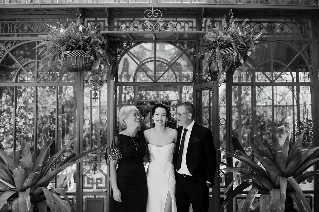 A newlywed with their parents on either side as they all smile 
