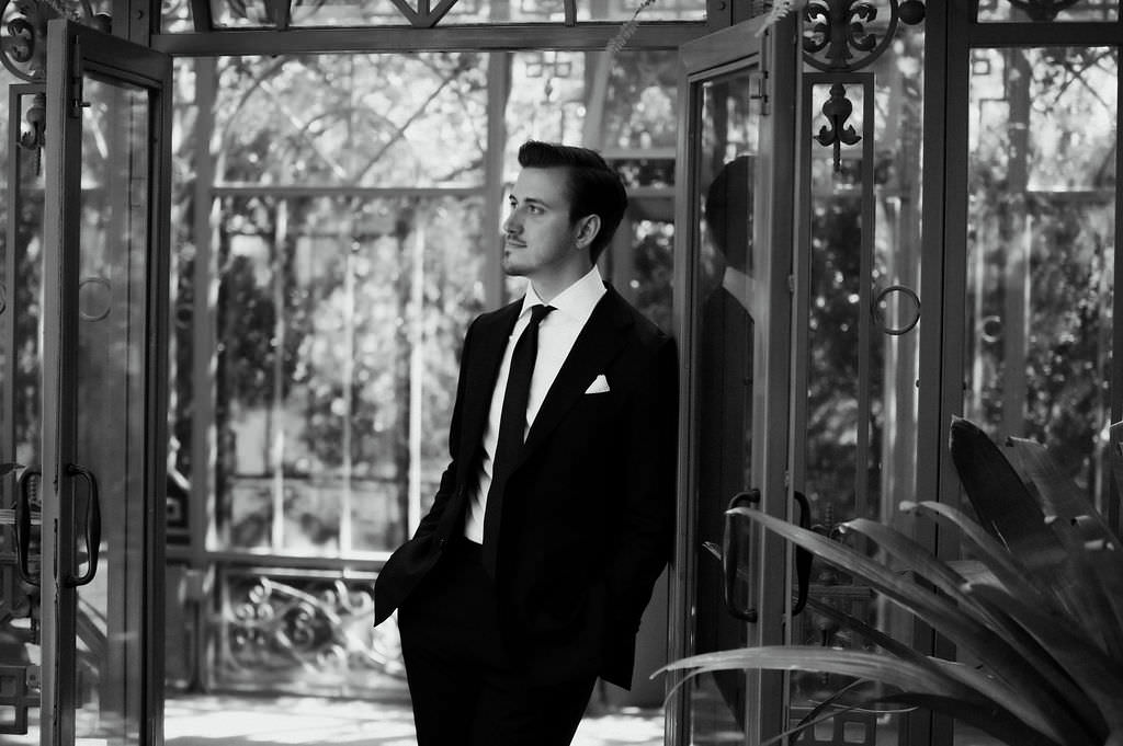 A person in a suit leaning against the door of a greenhouse 