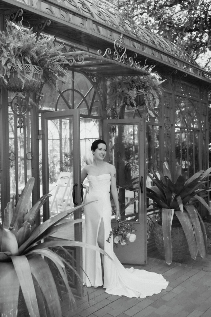 Black and white photo of a newlywed standing in the doorway of a greenhouse