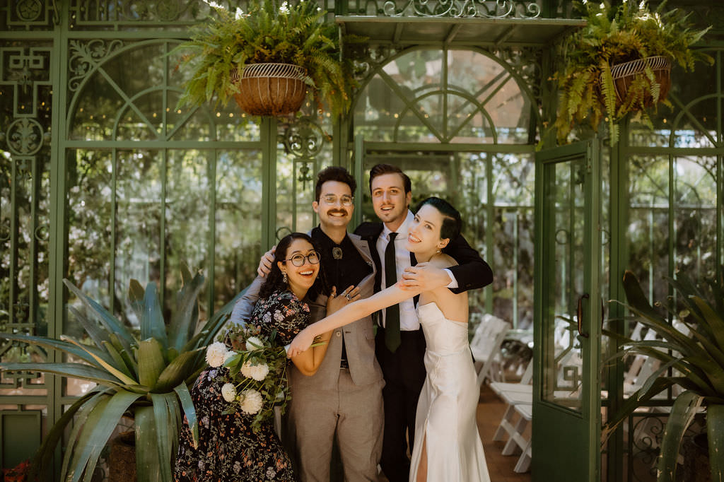 Newlyweds laughing with wedding guests as they throw their arms around each other 