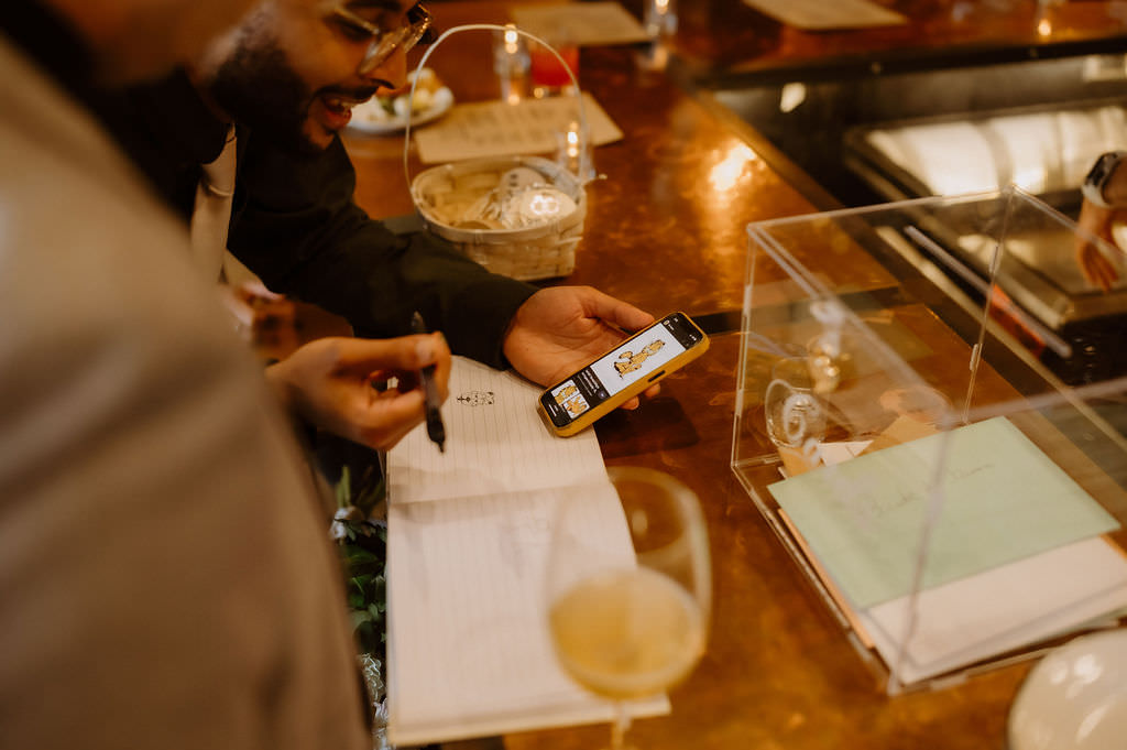 A wedding guests signing a book as they hold their phone out 