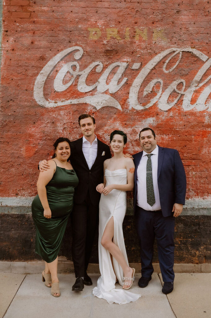 A wedding couple with guests on either side of them as they all smile 
