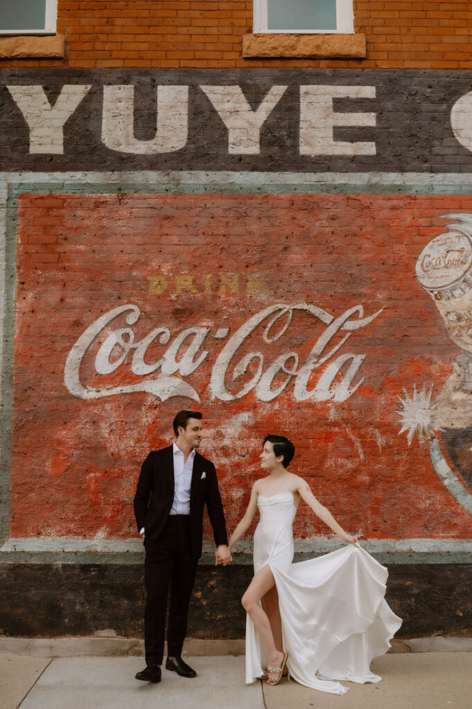 A newlywed couple standing in front of an old, painted brick building 