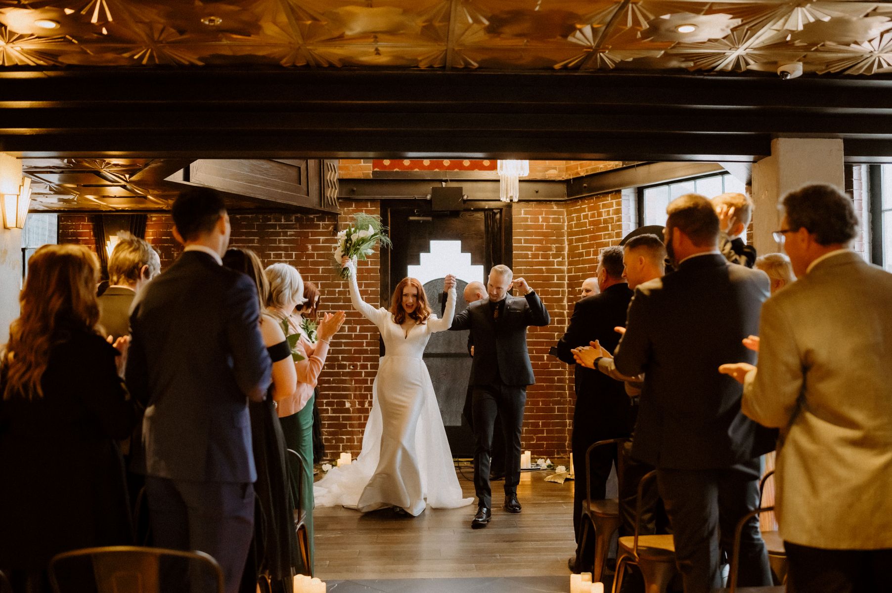 a couple making their entrance into their wedding and pumping their fists int he air their guests are standing and cheering for them