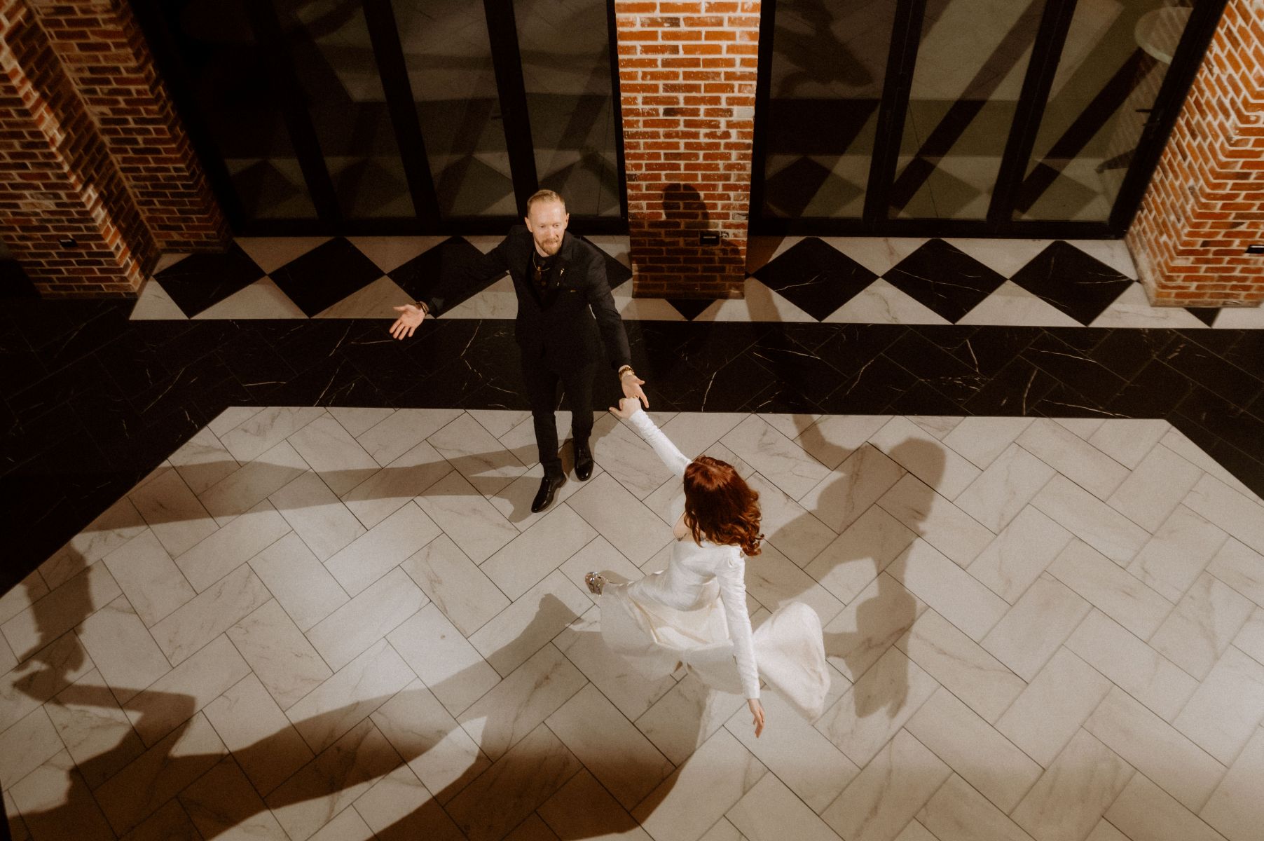 a couple on a dance floor dancing together the woman is wearing ahwite wedding dress and her partner who is wearing a black suit is spinning her 