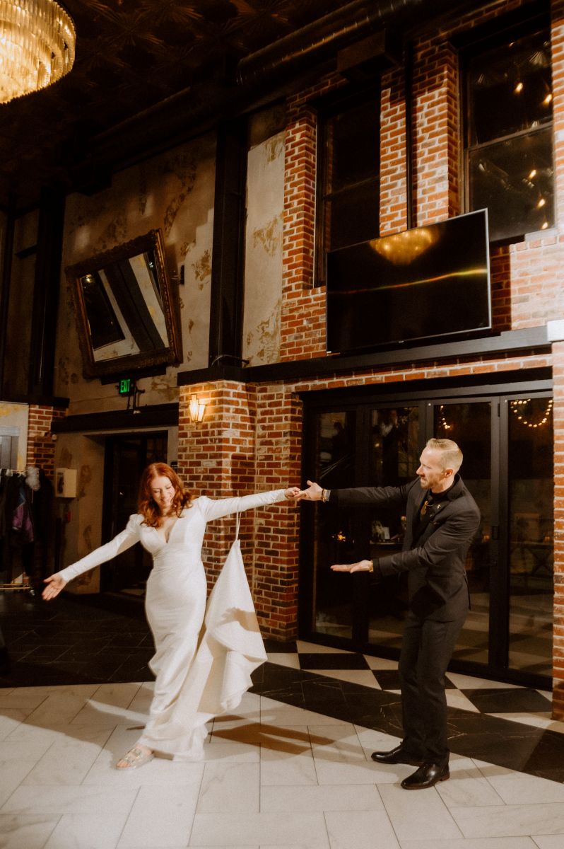 a couple on a dance floor together her partner who is wearing a black suit is holding her hand the woman is wearing a white wedding dress 