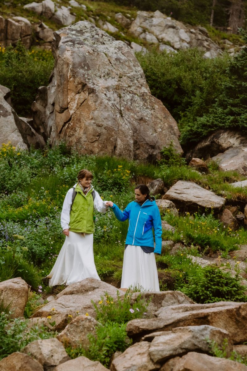 a couple helping each other climb over rocks one woman is wearing a green jacket the other woman is wearing a blue jacket 