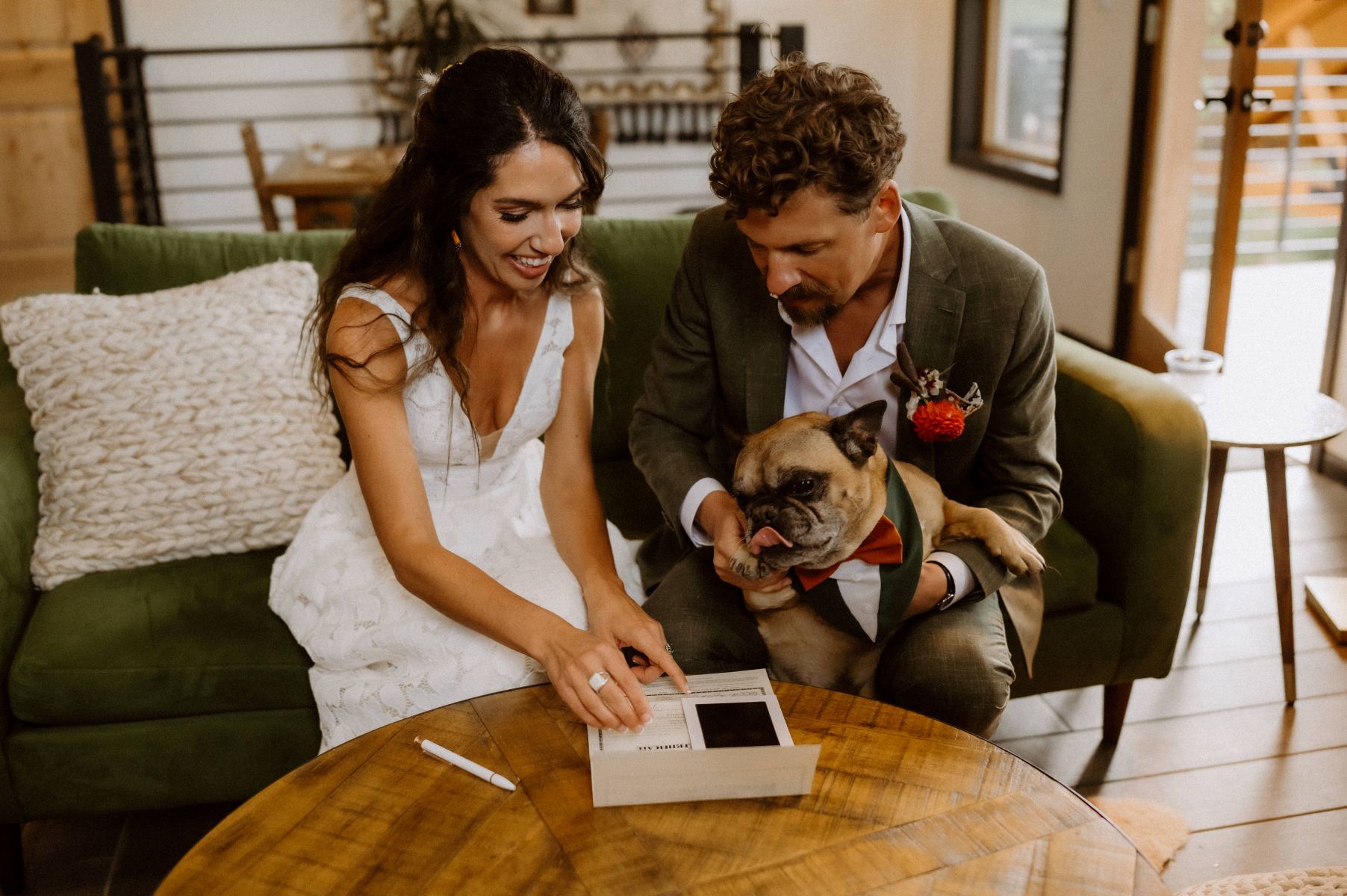a couple signing their marriage license with the man is holding their dog they are sitting on a green couch 
