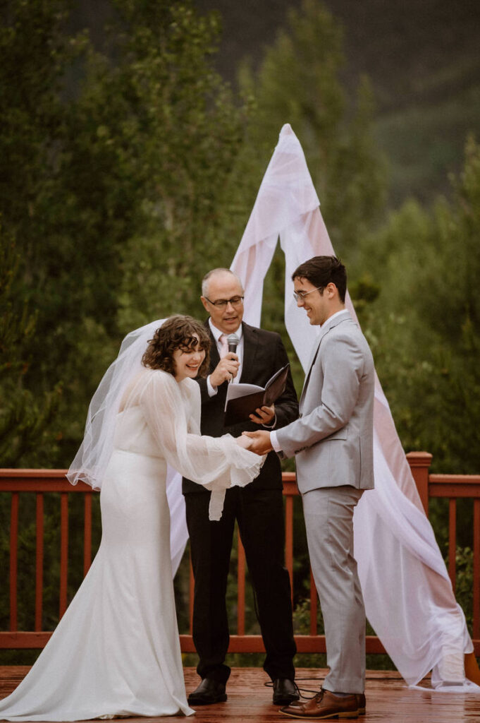 A couple holding hands and laughing as they say their vows 