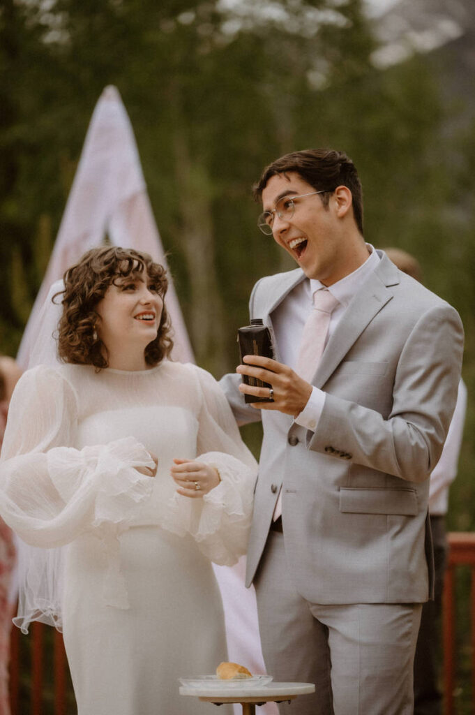 A couple laughing together and holding up a drink during their wedding ceremony 