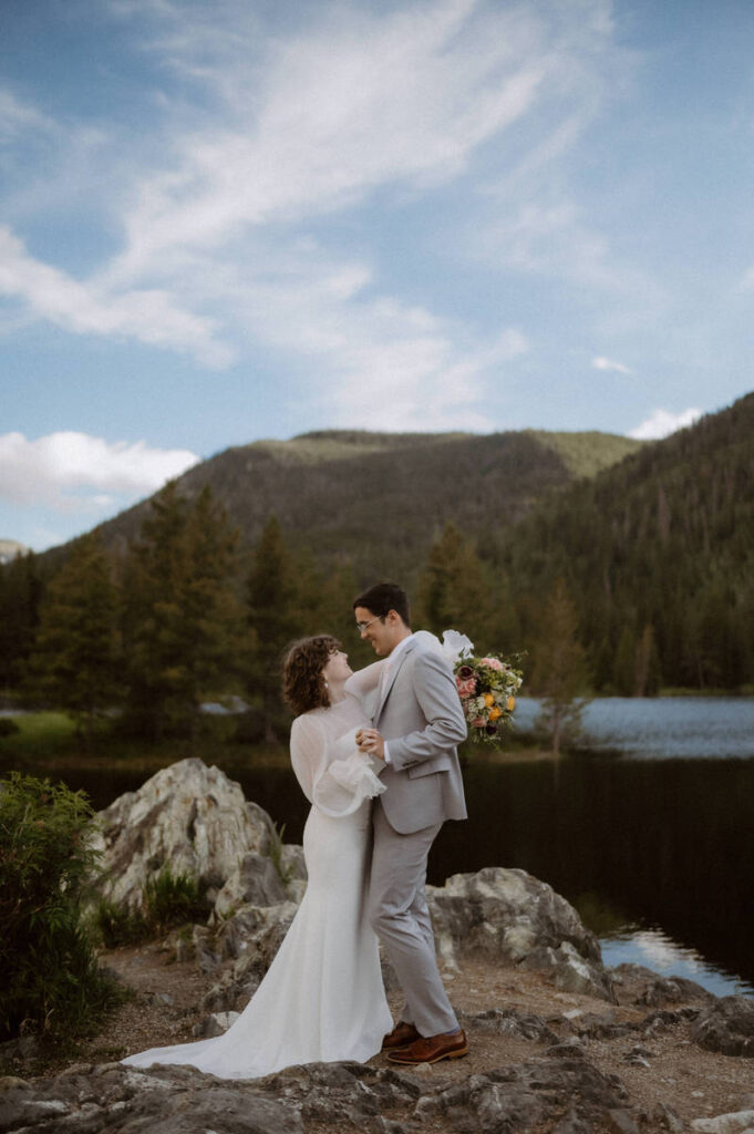 A newlywed couple dancing on a rock in front of a mountain lake 