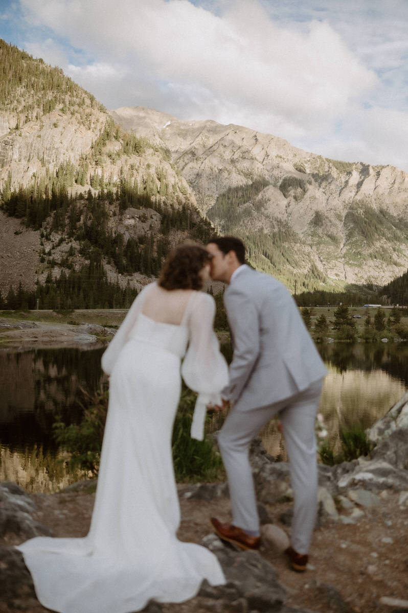 A newlywed couple leaning in to each other kissing in the mountains