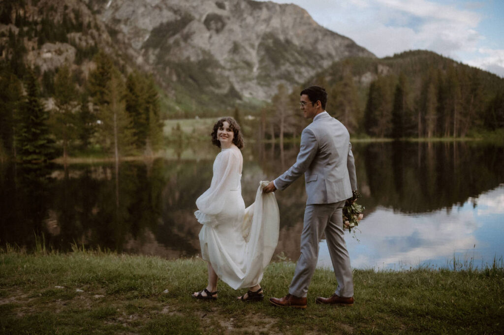 A person walking behind their partner holding up the end of their wedding dress 