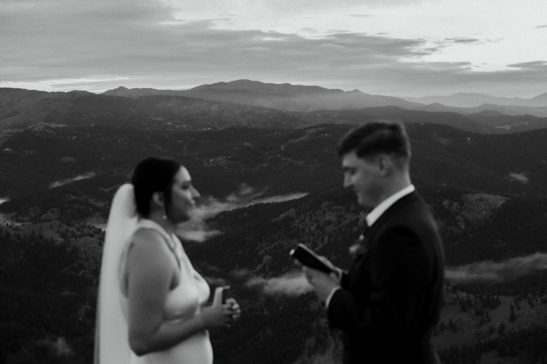 a couple reading vows to each other at lost gulch overlook in colorado during their elopement ceremony the woman is wearing a white dress and veil the man is wearing a black suit