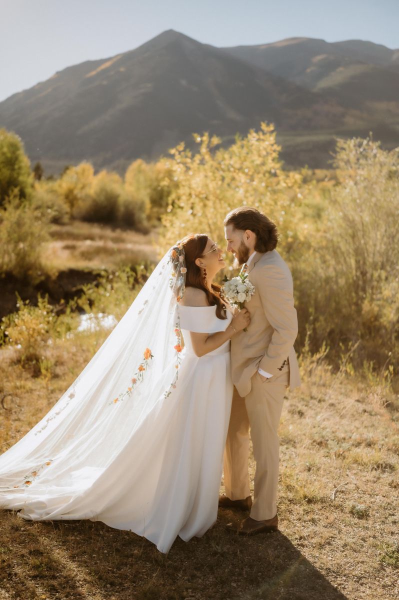 a couple having their wedding ceremony at twin lakes in colorado at sunset the woman is wearing a white wedding dress and holding flowers the man is wearing a tan suit 
