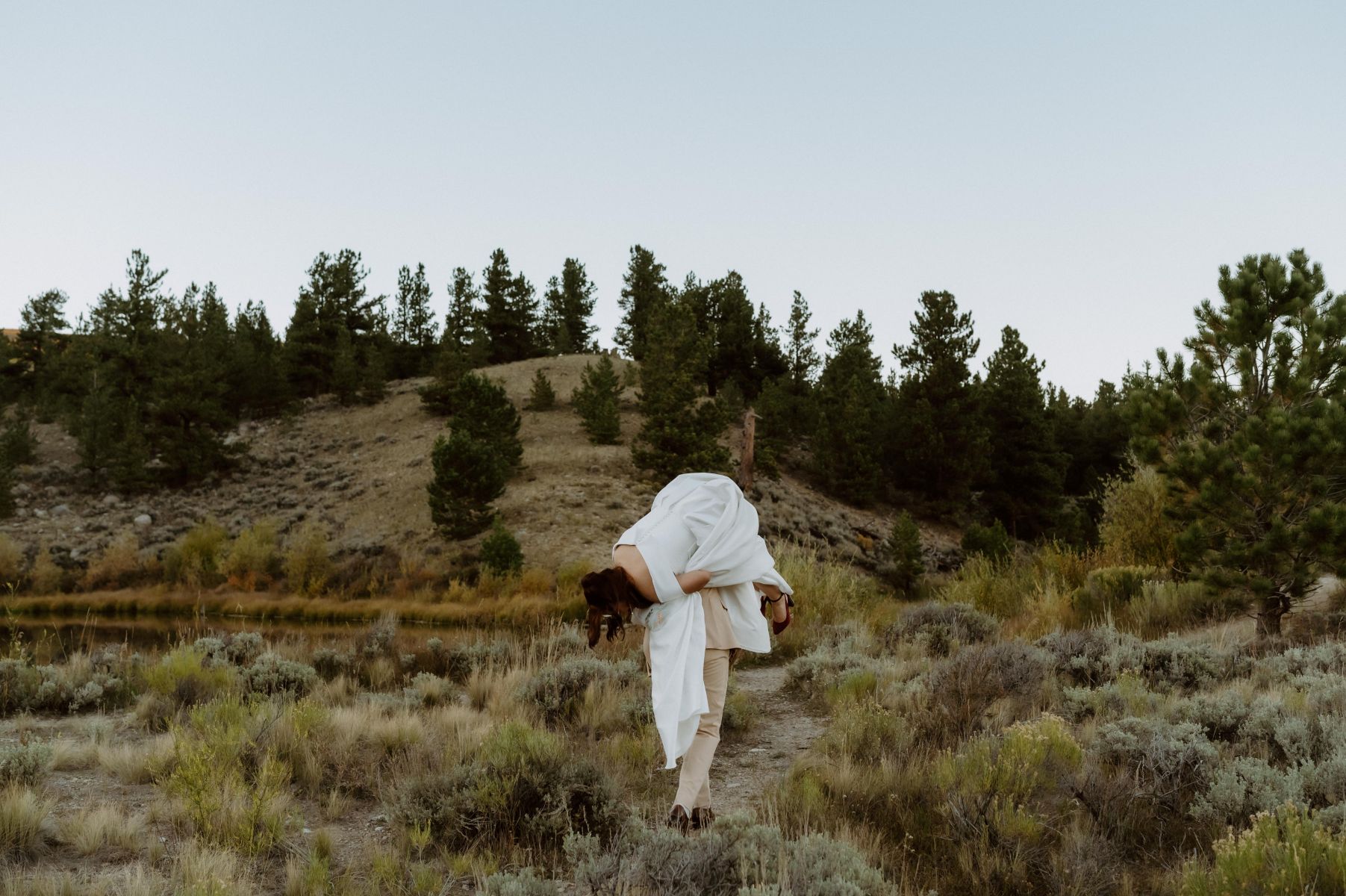 a man picking up his partner and putting her over his shoulder as they walk down a path together 