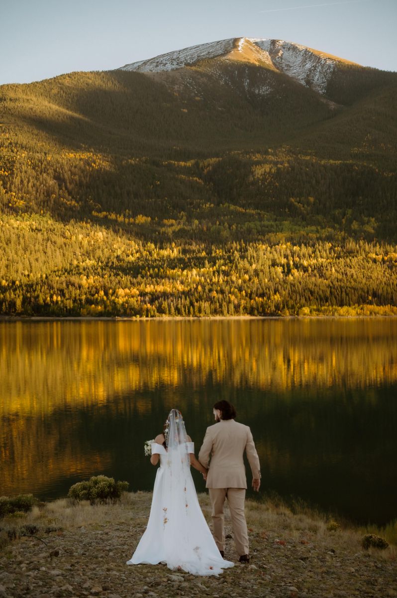 a couple standing next to twin lakes in colorado holding hands and looking out to the lake as the sun sets 